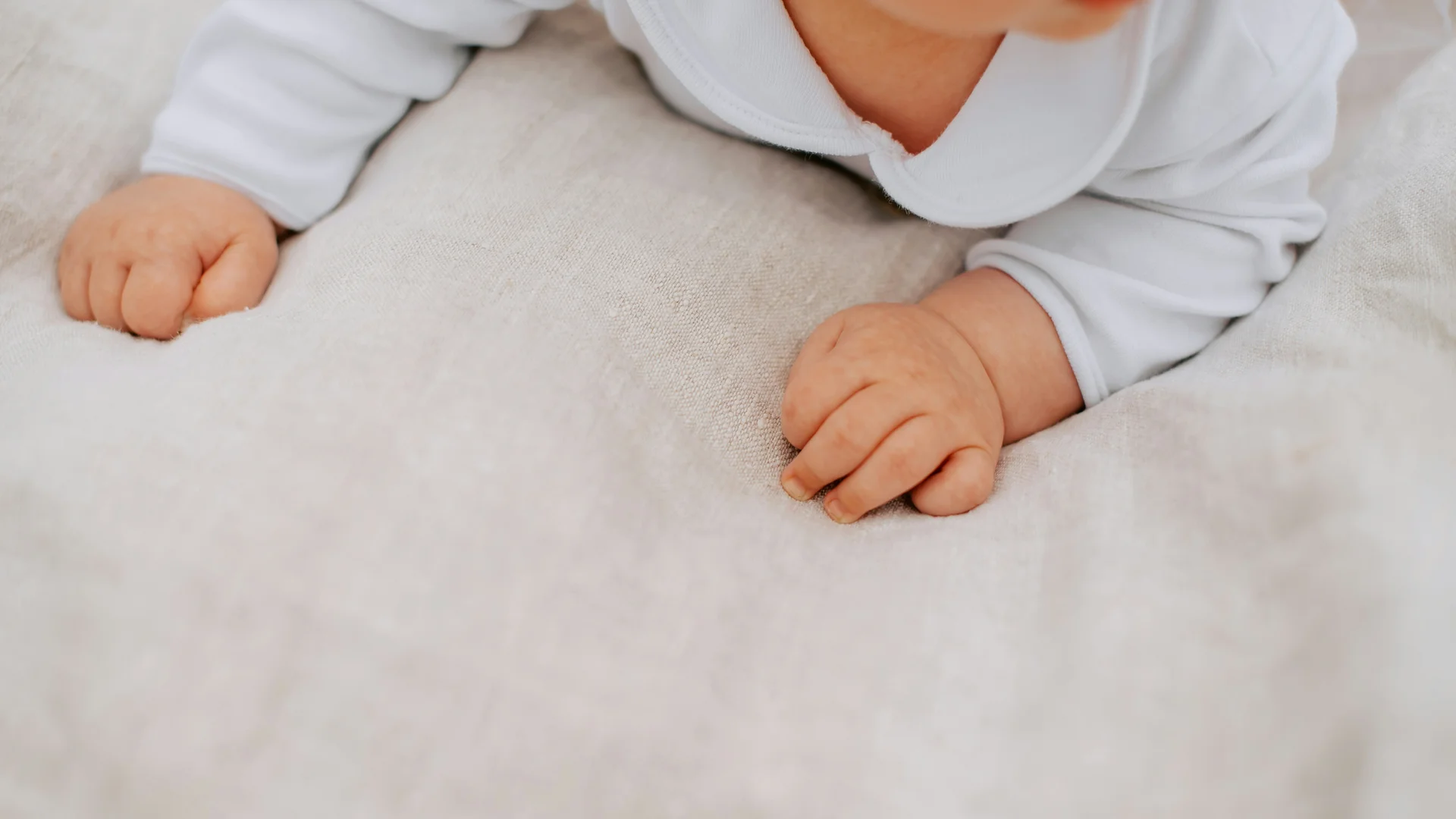 Familienurlaub mit Baby und Kleinkind im Buchau Nahaufnahme der Hände eines Babys auf einer hellen Decke in weißer Kleidung