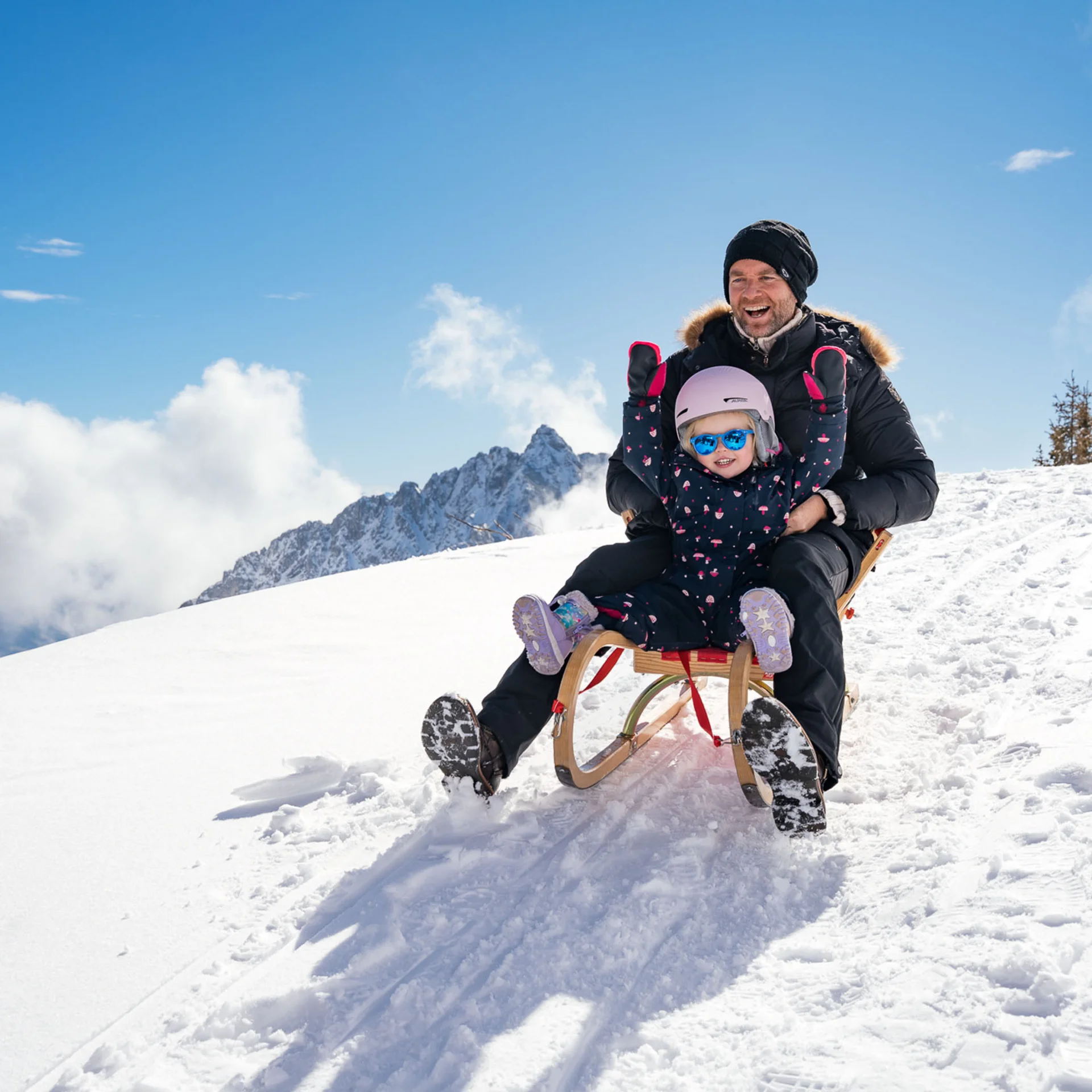 Familienzeit im Kinderhotel Buchau am Achensee Vater und Kind rodeln glücklich im Schnee auf einem sonnigen Berg