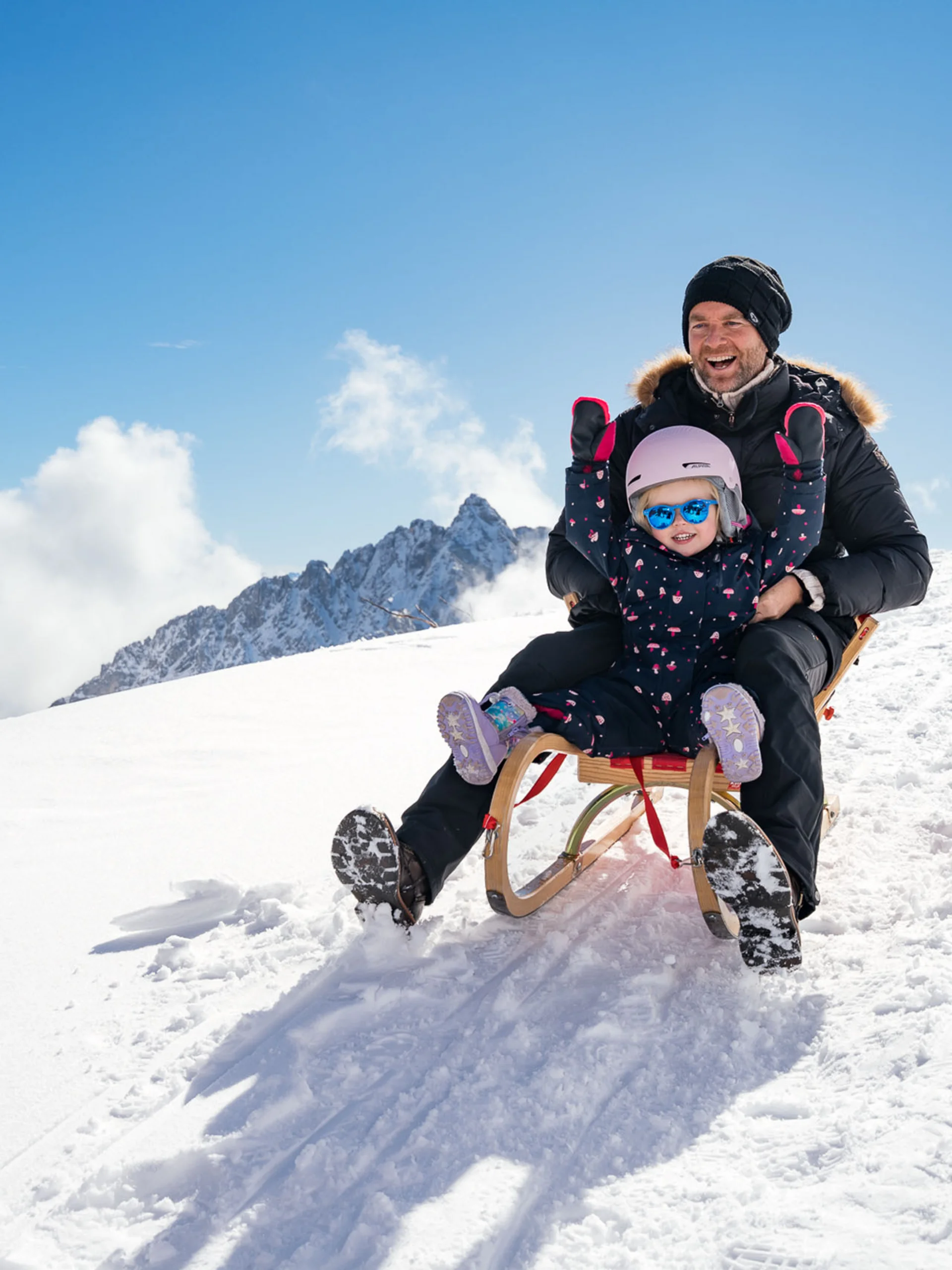 Willkommen im Familienhotel Buchau am Achensee Vater und Kind rodeln glücklich im Schnee auf einem sonnigen Berg
