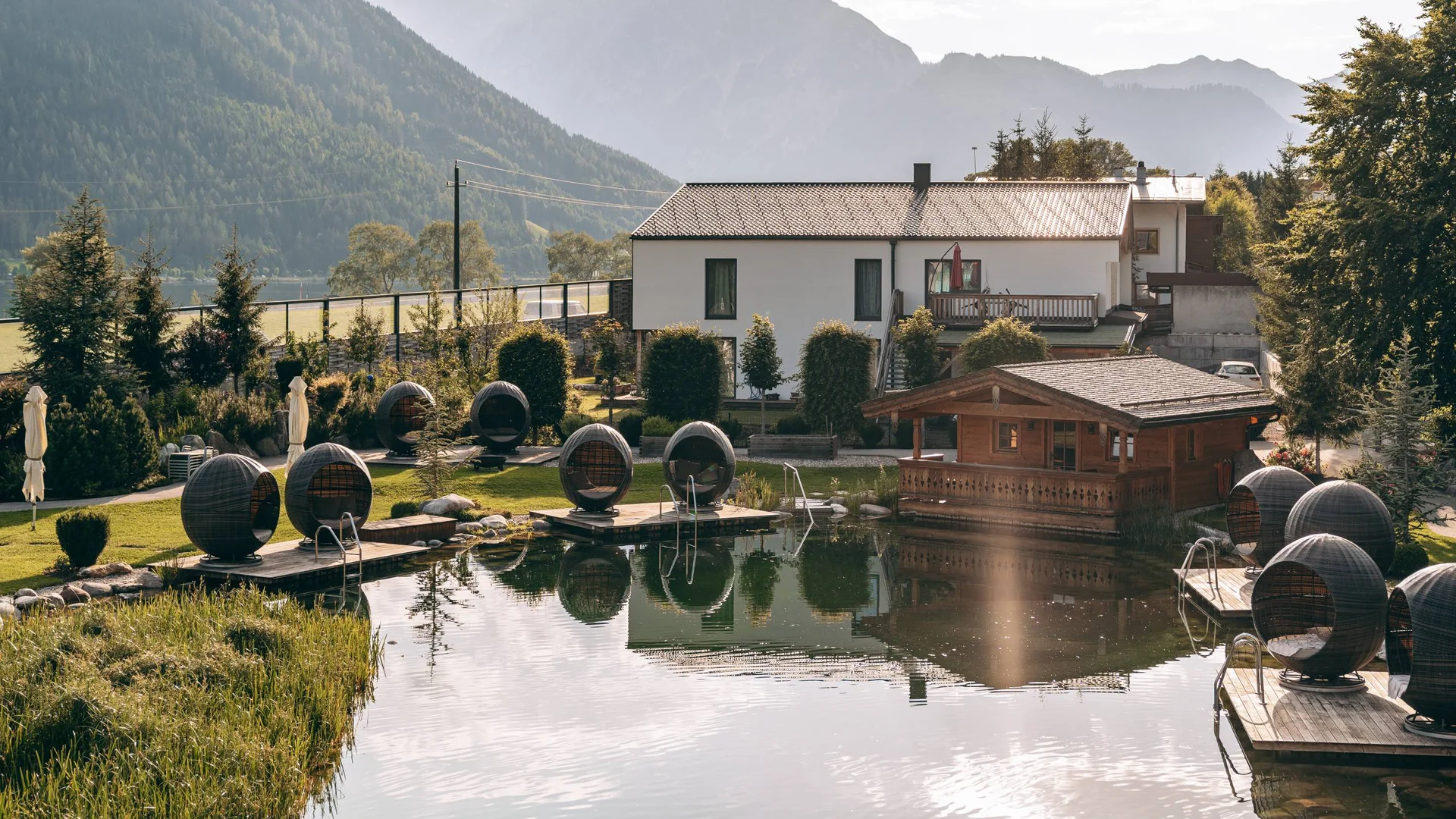 Urlaub im Wellnesshotel mit Kindern in Tirol Haus und Holzpavillon am Teich mit Sitzkugeln und Bergblick