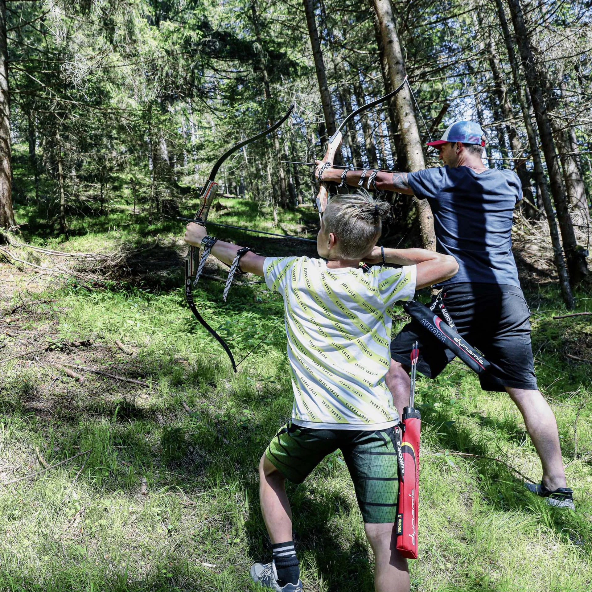 Familienzeit im Kinderhotel Buchau am Achensee Zwei Menschen beim Bogenschießen im Wald auf eine Vogelattrappe