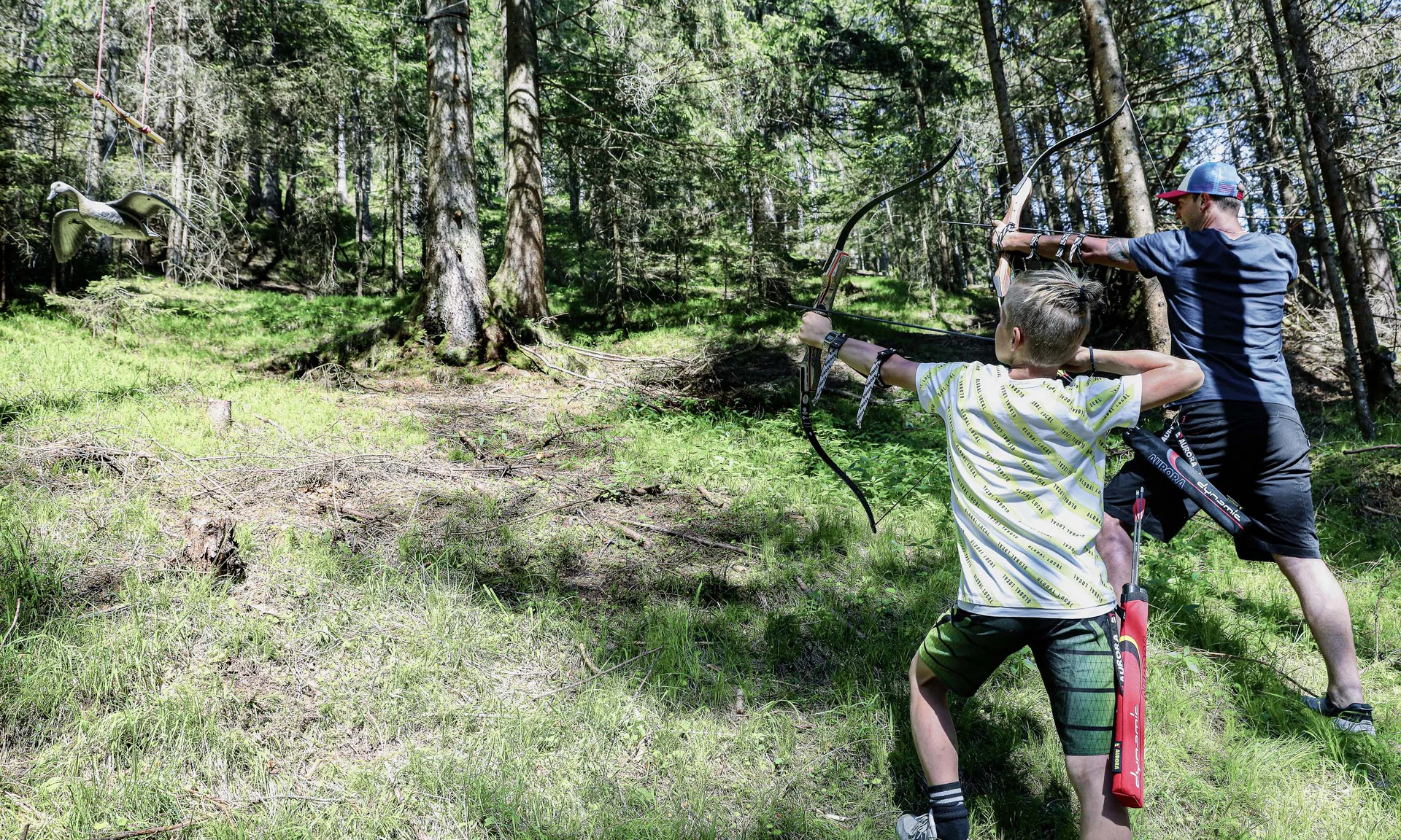 Outdoorspaß im Familienhotel am See in Österreich Zwei Menschen beim Bogenschießen im Wald auf eine Vogelattrappe