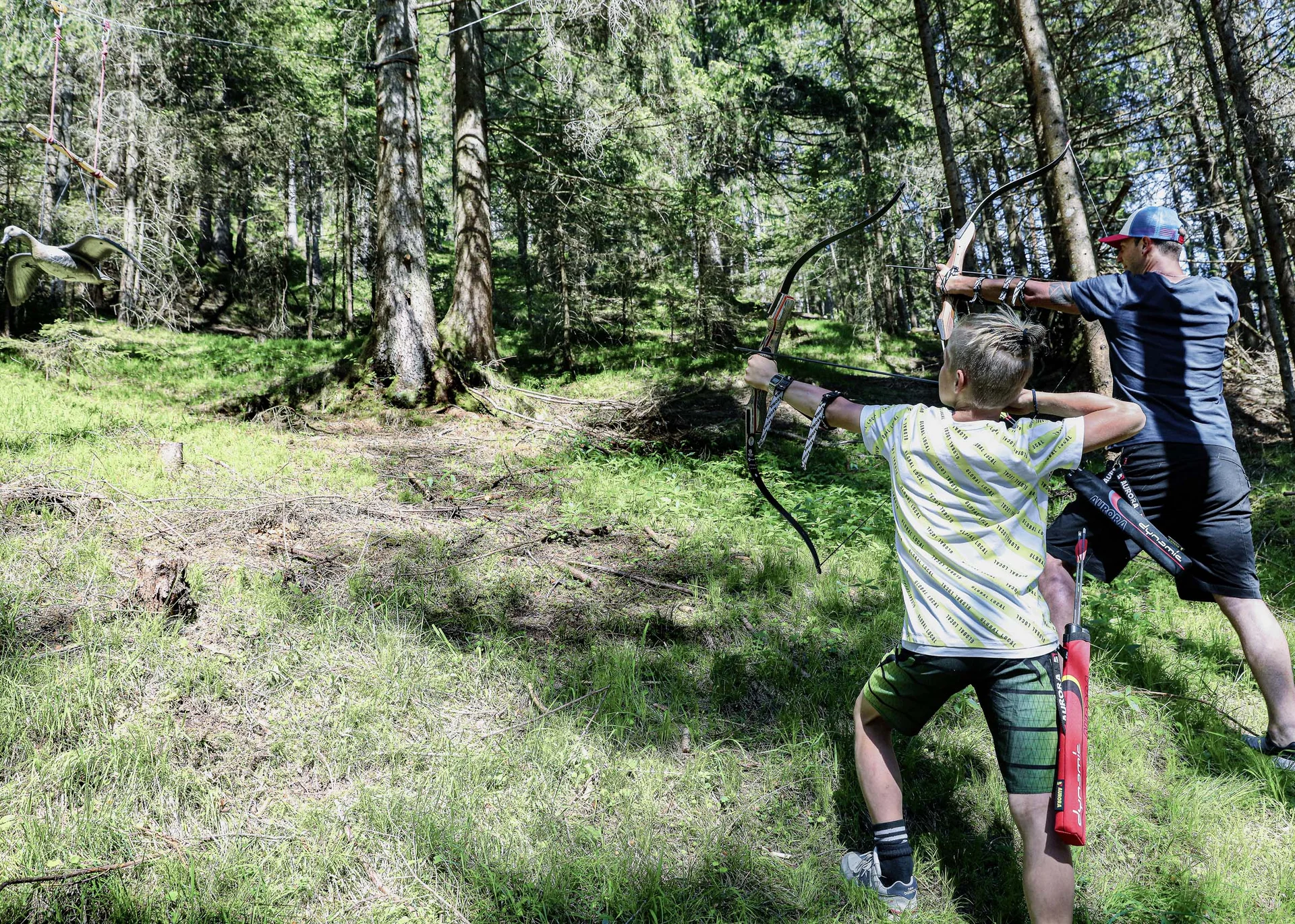 Ihr abenteuerlicher Erlebnisurlaub in Österreich Zwei Menschen beim Bogenschießen im Wald auf eine Vogelattrappe