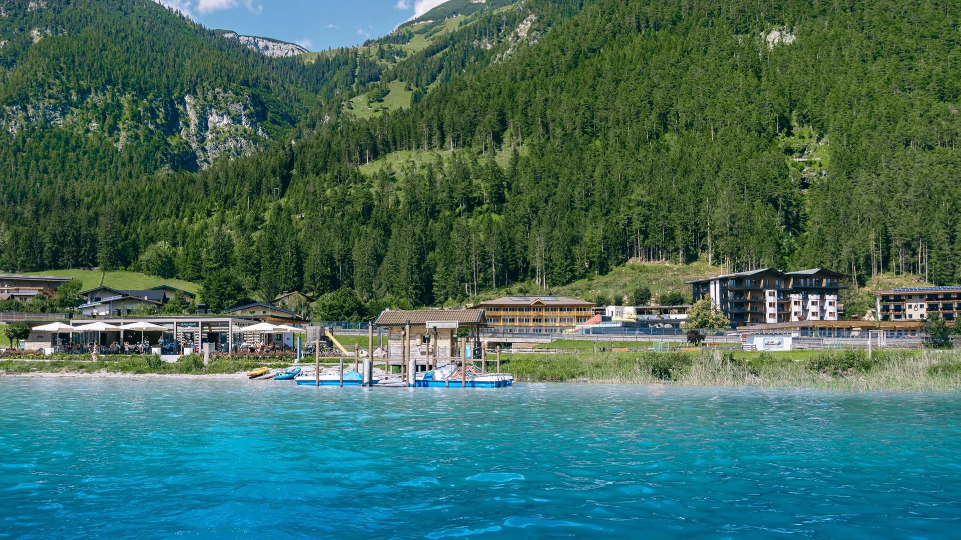 Wassersport auf dem See in Österreich Klares blaues Wasser mit Bergkulisse und Gebäude am Ufer bei sonnigem Wetter