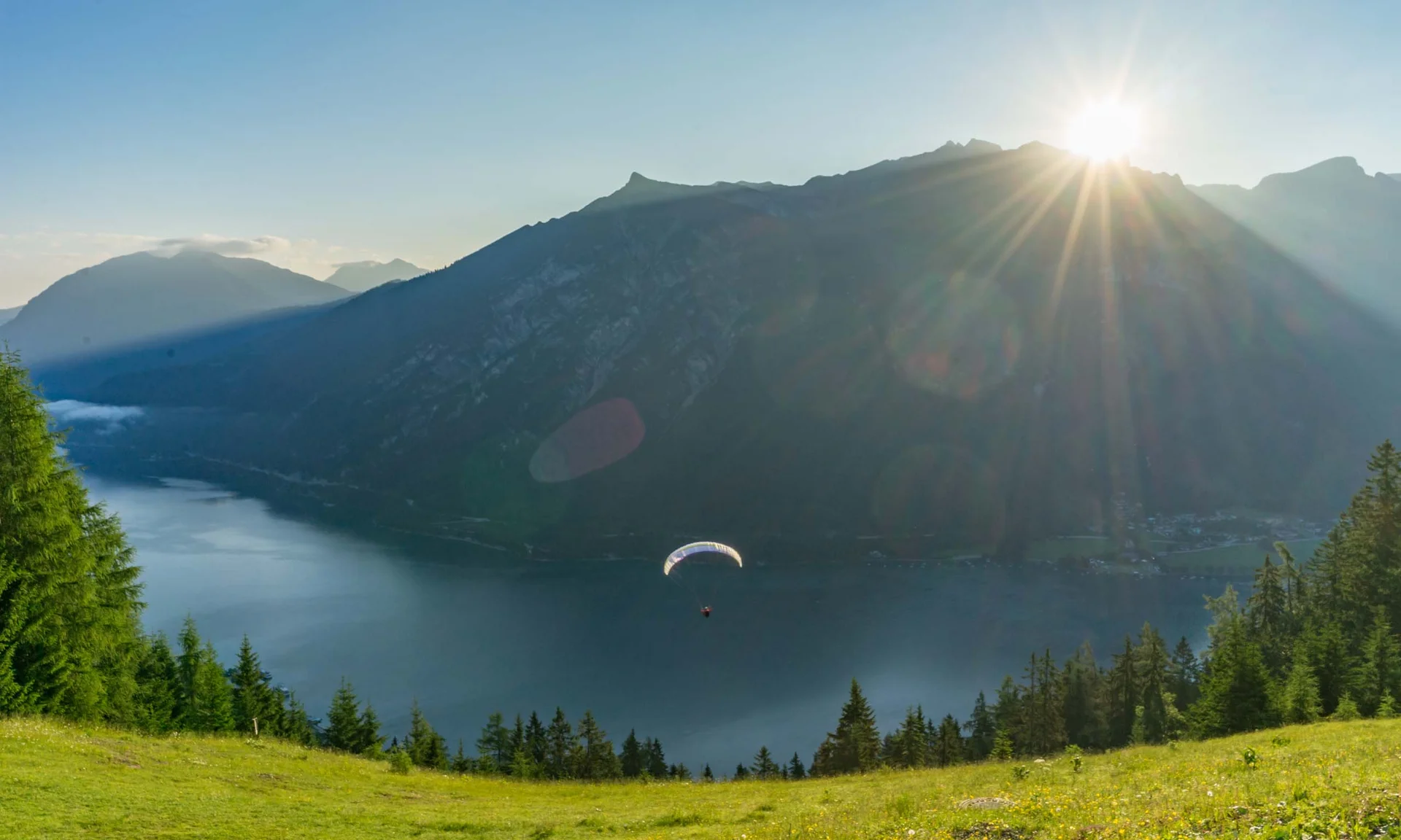 Your unforgettable active lakeside holiday in Austria Paraglider flying over lake with mountains and sunset in the background