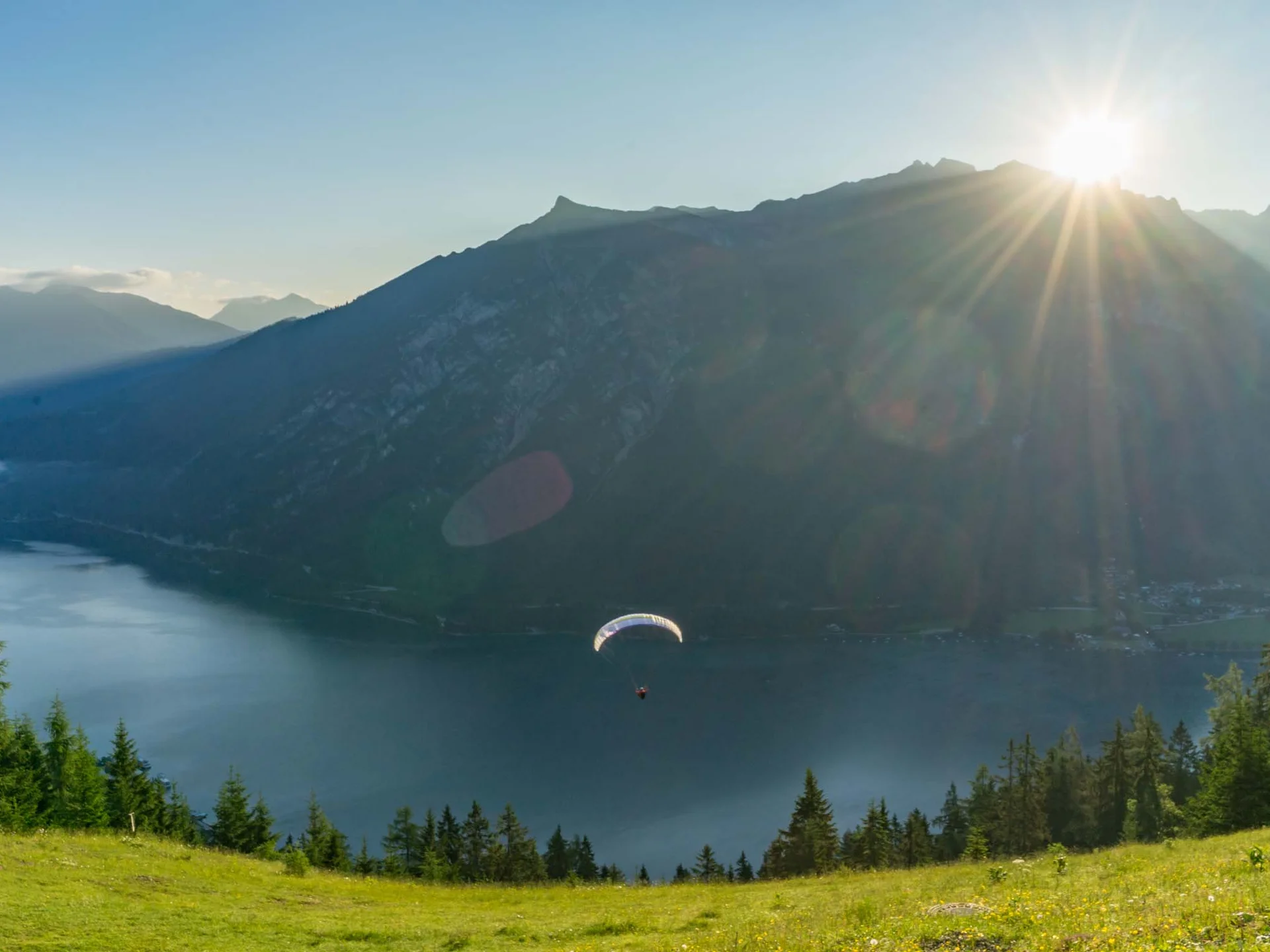 Your unforgettable active lakeside holiday in Austria Paraglider flying over lake with mountains and sunset in the background