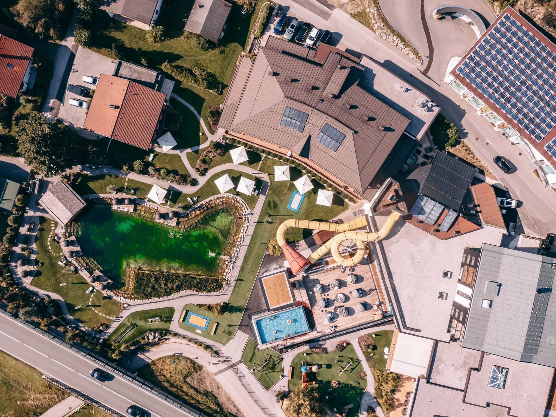 Outdoorspaß im Familienhotel am See in Österreich Luftaufnahme eines Freizeitbads mit Wasserrutschen, Schwimmbecken und Grünflächen