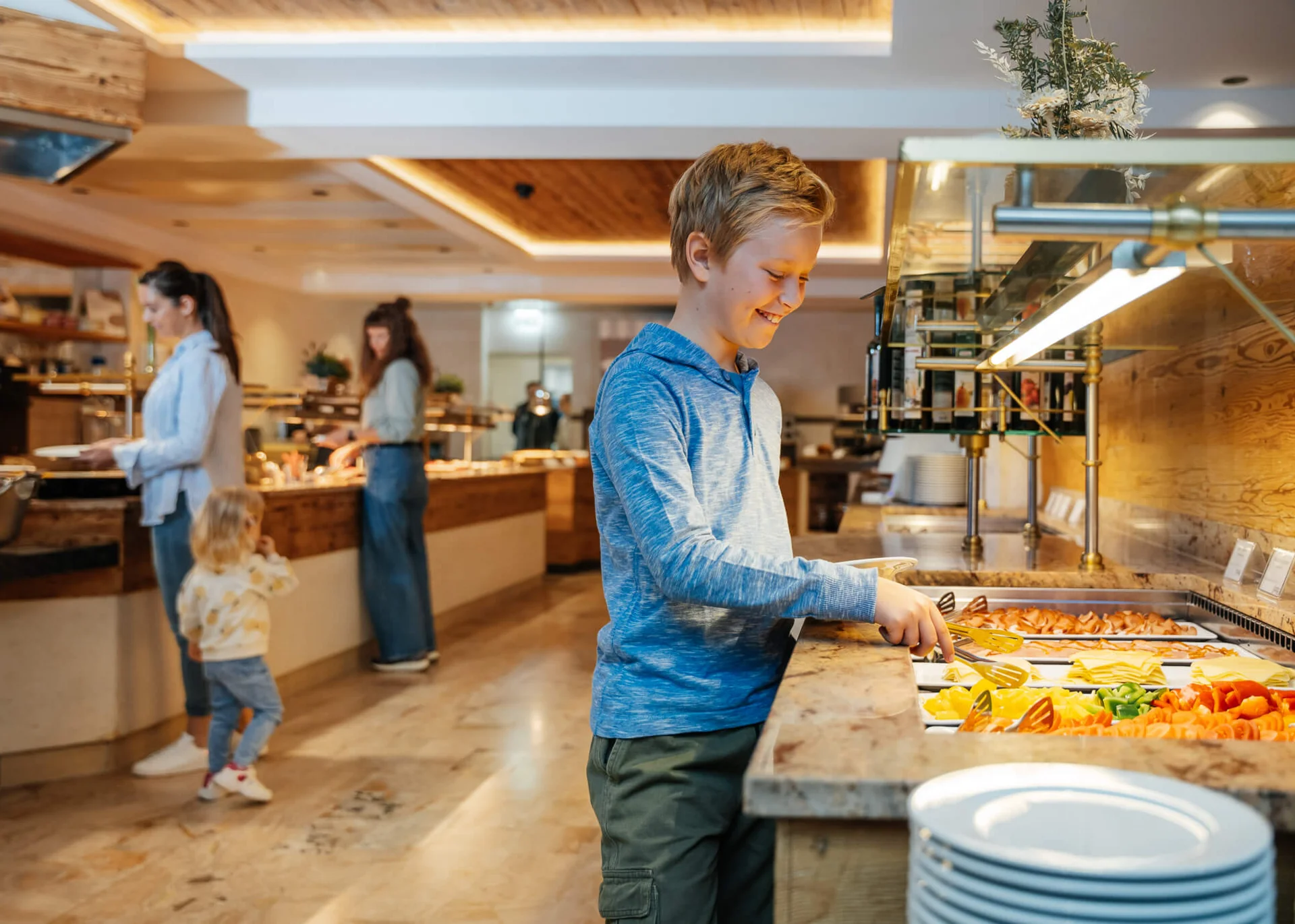 Ihr Hotel für Alleinerziehende Junge nimmt Essen vom Buffet in einem Restaurant mit Familien im Hintergrund