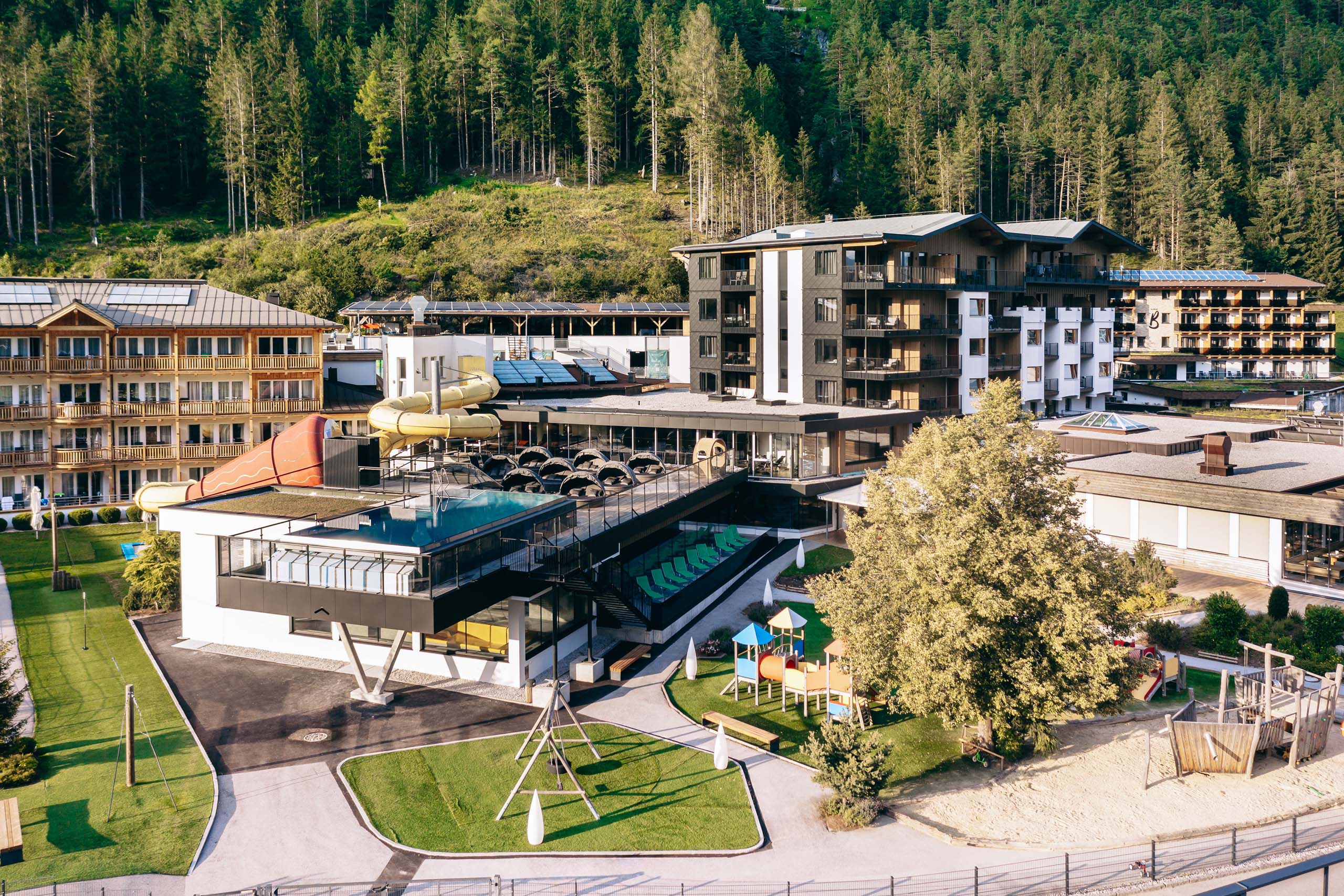 Wir lassen Bilder sprechen. Hotel mit Wasserrutsche, Pool, Spielplatz und Wald im Hintergrund