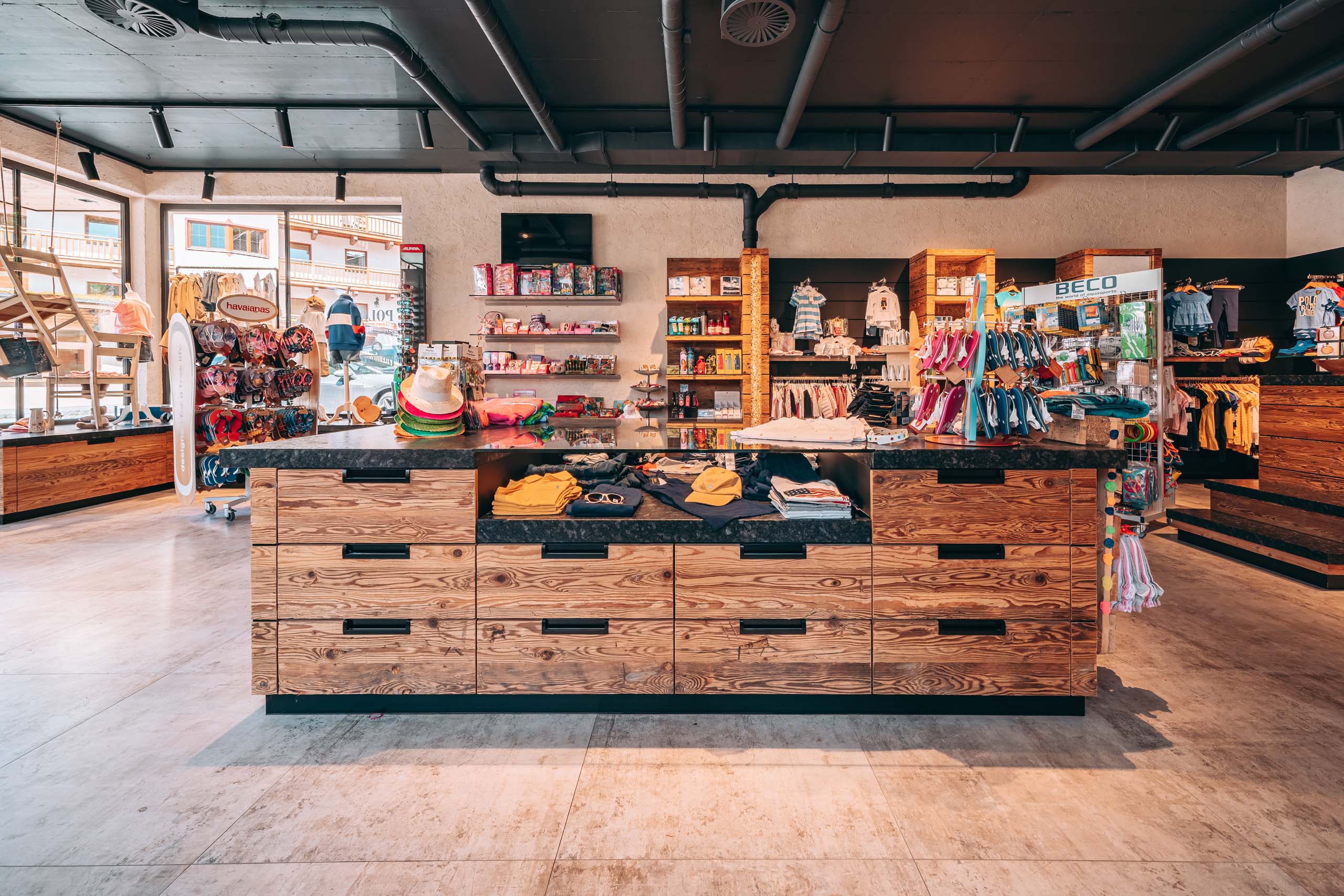 Wir lassen Bilder sprechen. Innenansicht eines Bekleidungsgeschäfts mit Holztheke und Regalen voller Kleidung und Accessoires