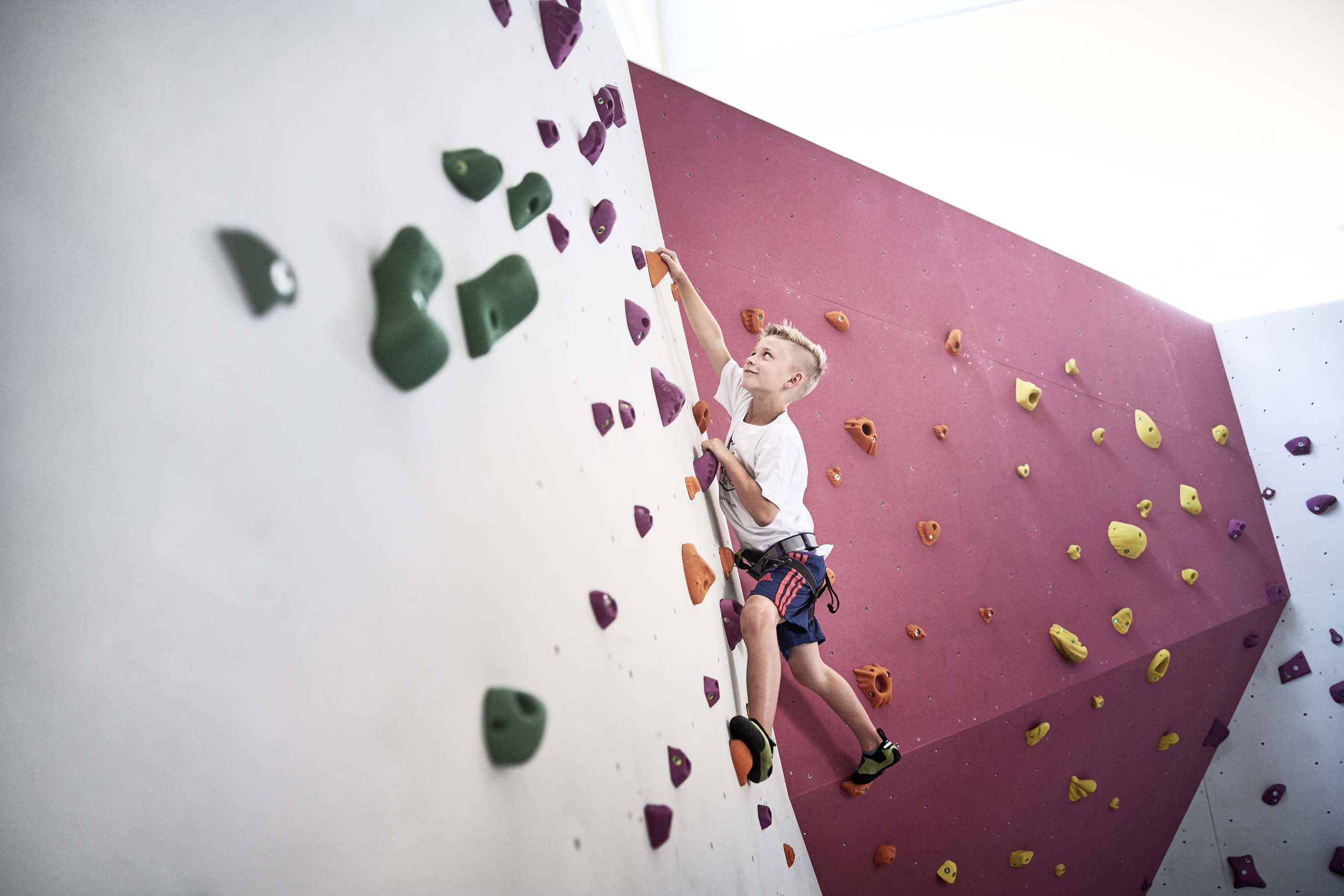 Familienzeit im Kinderhotel Buchau am Achensee Kind klettert an einer farbigen Indoor-Kletterwand mit Sicherungsgurt