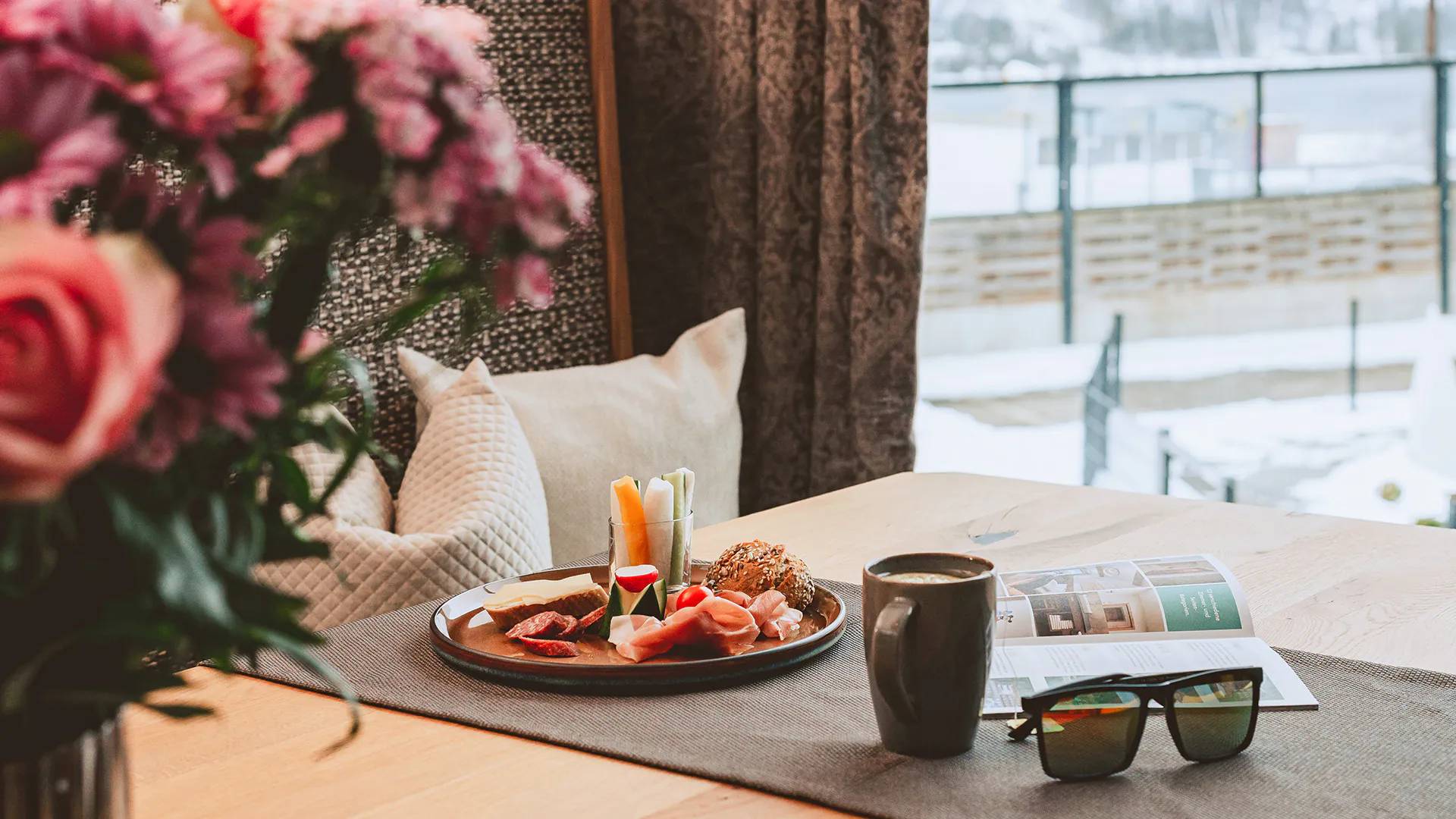 Wir lassen Bilder sprechen. Frühstück mit Wurst, Käse, Gemüse, Kaffee und Buch auf Tisch mit Blumen