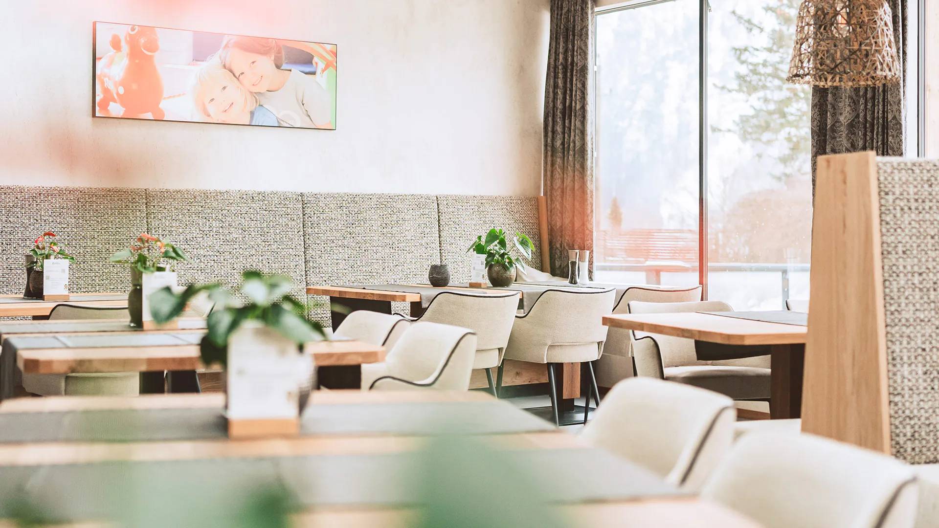 Wir lassen Bilder sprechen. Helles modernes Restaurant mit Grau- und Holztönen, Pflanzen und Bilderrahmen an der Wand