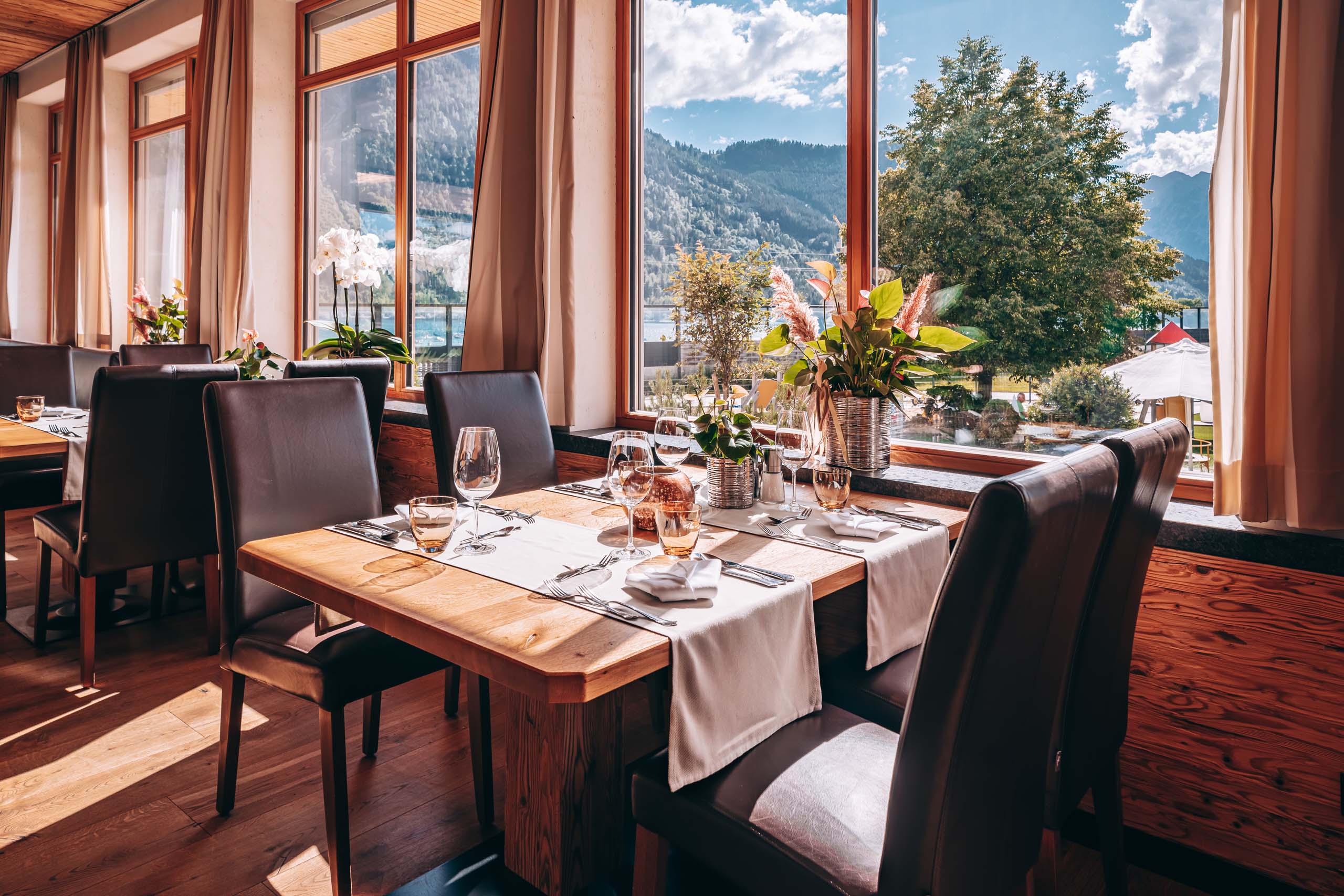 Wir lassen Bilder sprechen. Restaurant mit modernem Holztisch, Ledersesseln und Bergblick durch große Fenster