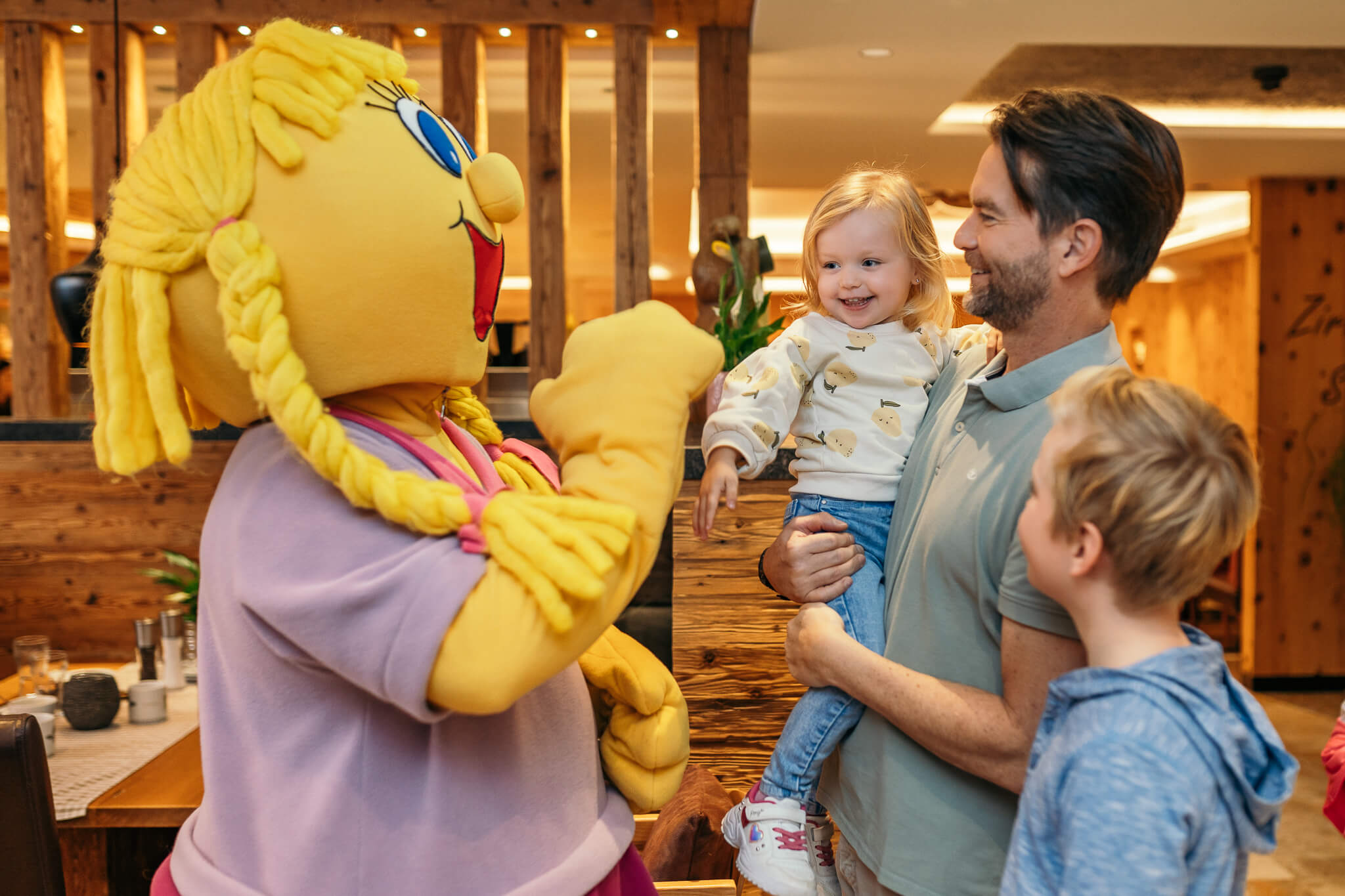 Familien Wellness Tage mit tollen Vorteilen Kind lacht, während es mit einem gelben Maskottchen im Restaurant interagiert