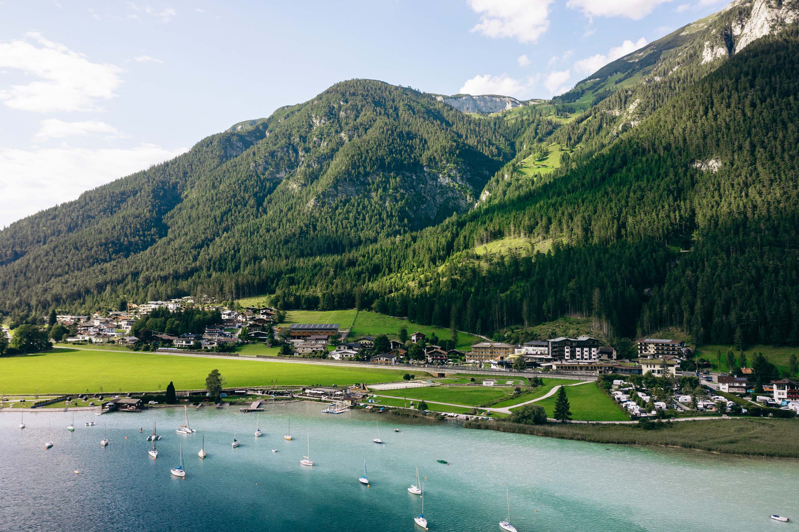 Wir lassen Bilder sprechen. Blick auf einen kleinen Ort am See vor bewaldeten Bergen bei klarem Wetter