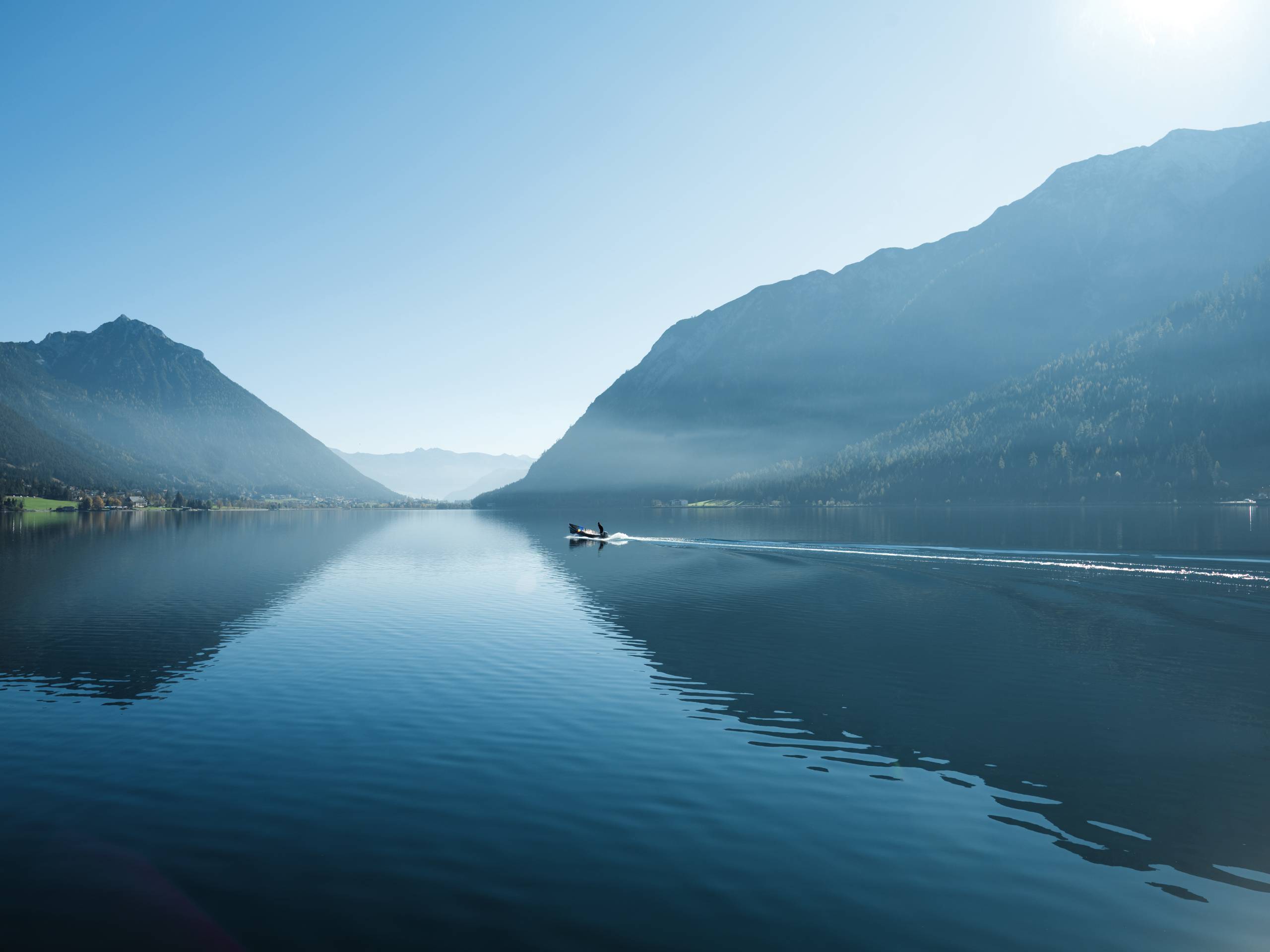 Wassersport auf dem See in Österreich Boot fährt auf ruhigem See zwischen Bergen an klar blauem Himmel