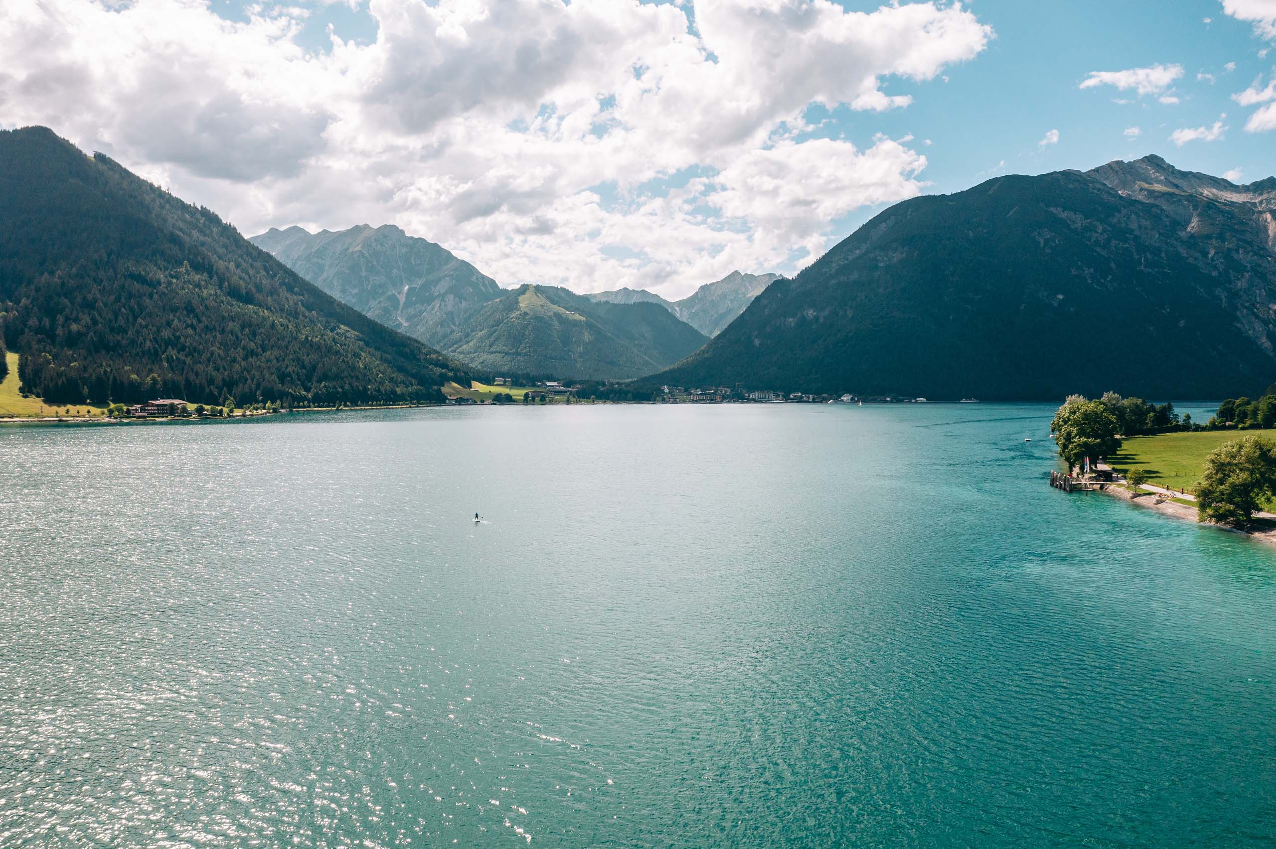 Wir lassen Bilder sprechen. Blauer Bergsee umgeben von bewaldeten Bergen unter bewölktem Himmel