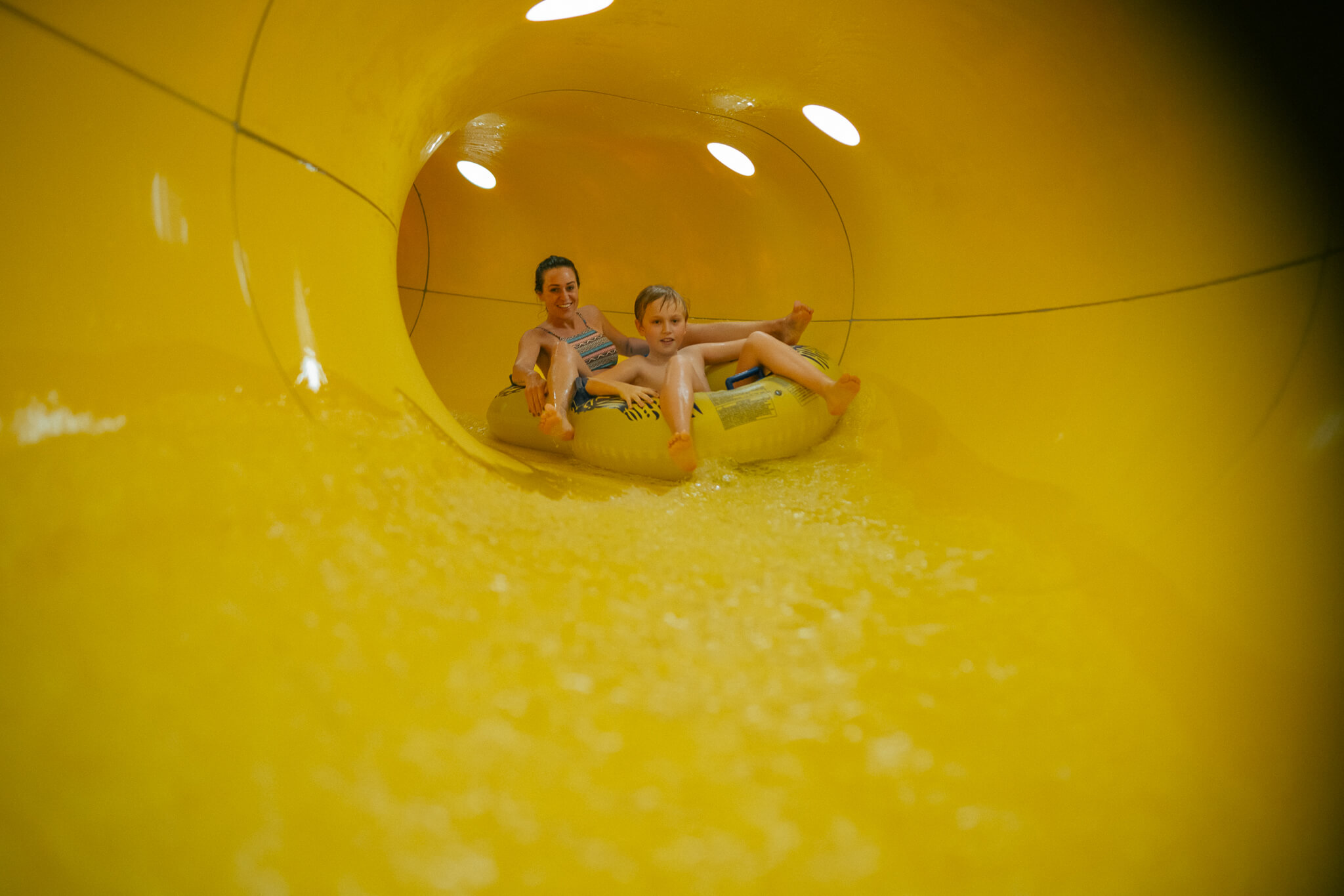 Wasserspaß im Familienhotel in Tirol mit Pool Mutter und Sohn fahren gemeinsam auf einem Schlauchreifen in einer gelben Wasserrutsche