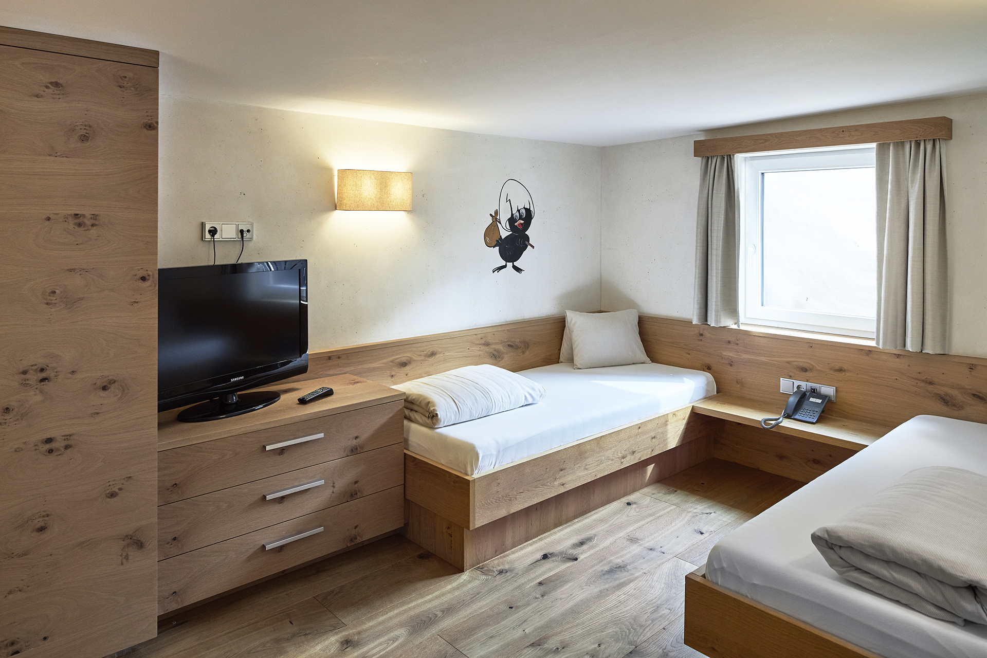 Wir lassen Bilder sprechen. Hell eingerichtetes Hotelzimmer mit zwei Holzbetten, Fernseher und Wandbild