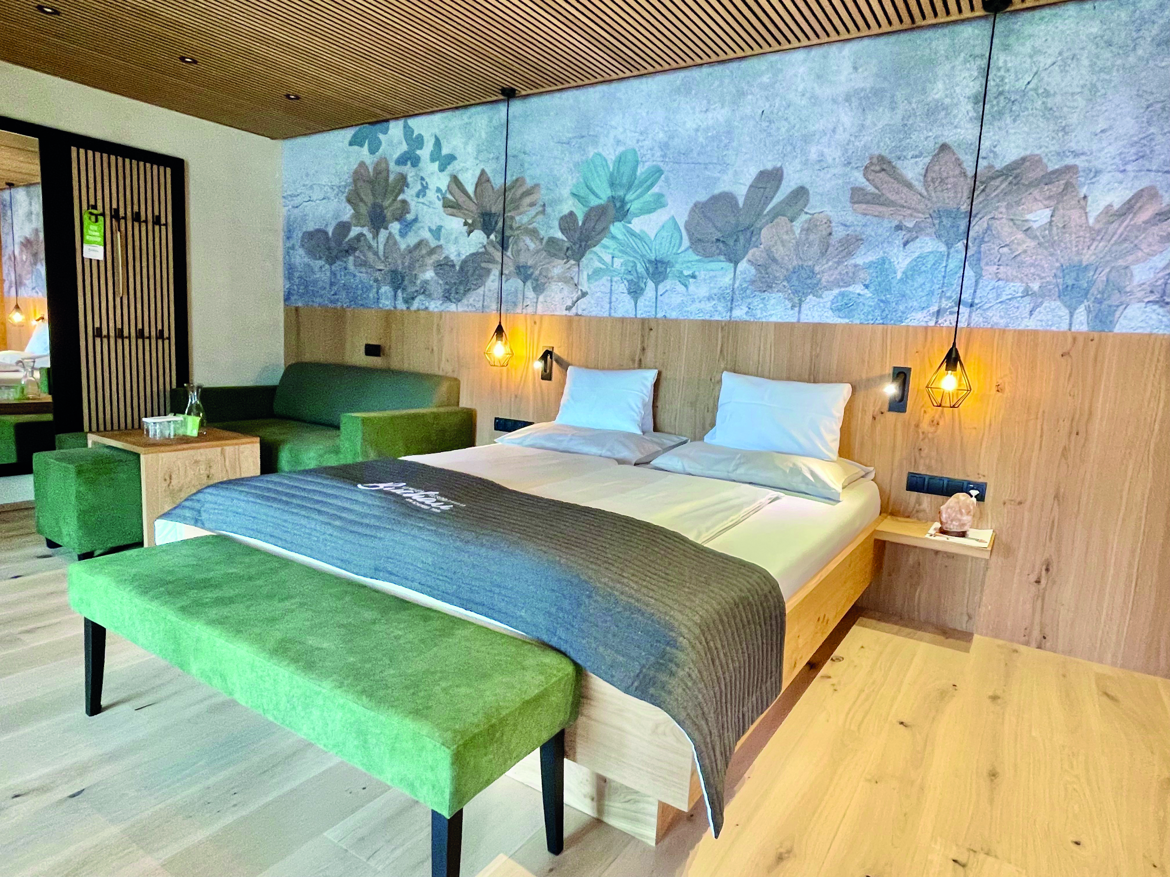Wir lassen Bilder sprechen. Modernes Hotelzimmer mit Doppelbett, grüner Sitzbank und floralem Wandbild