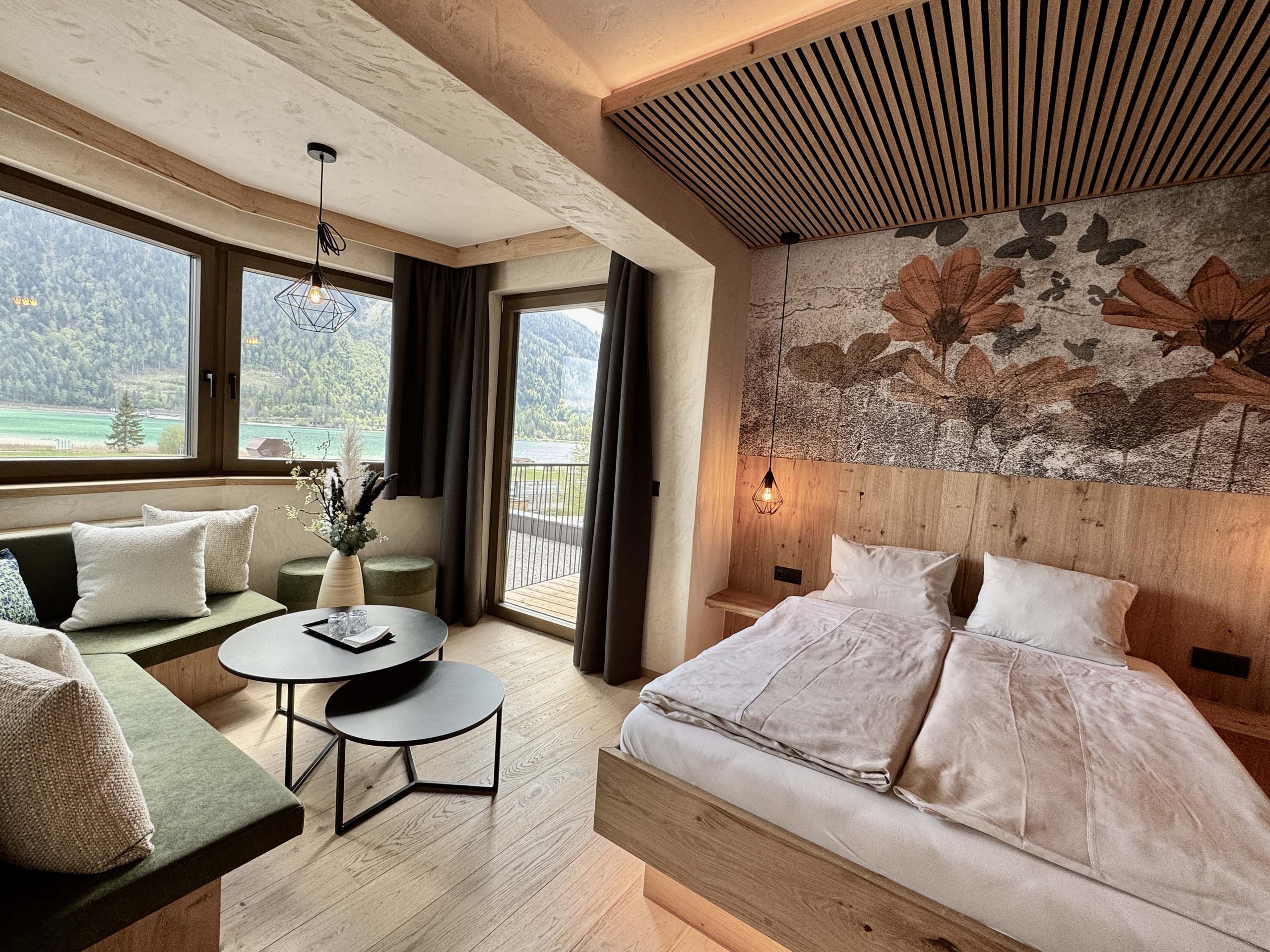 Wir lassen Bilder sprechen. Gemütliches Hotelzimmer mit Doppelbett, Sitzbereich und Bergblick durch große Fenster