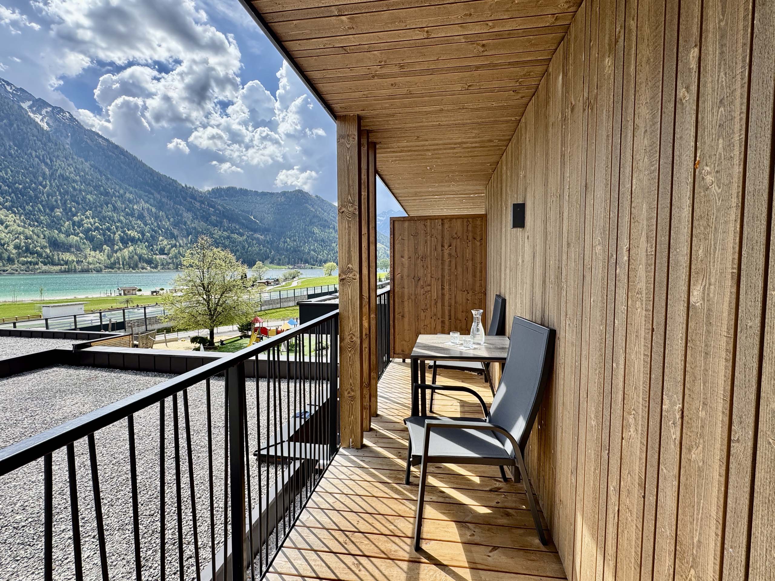 Wir lassen Bilder sprechen. Balkon mit Stühlen und Tisch mit Aussicht auf See und Berge bei sonnigem Wetter