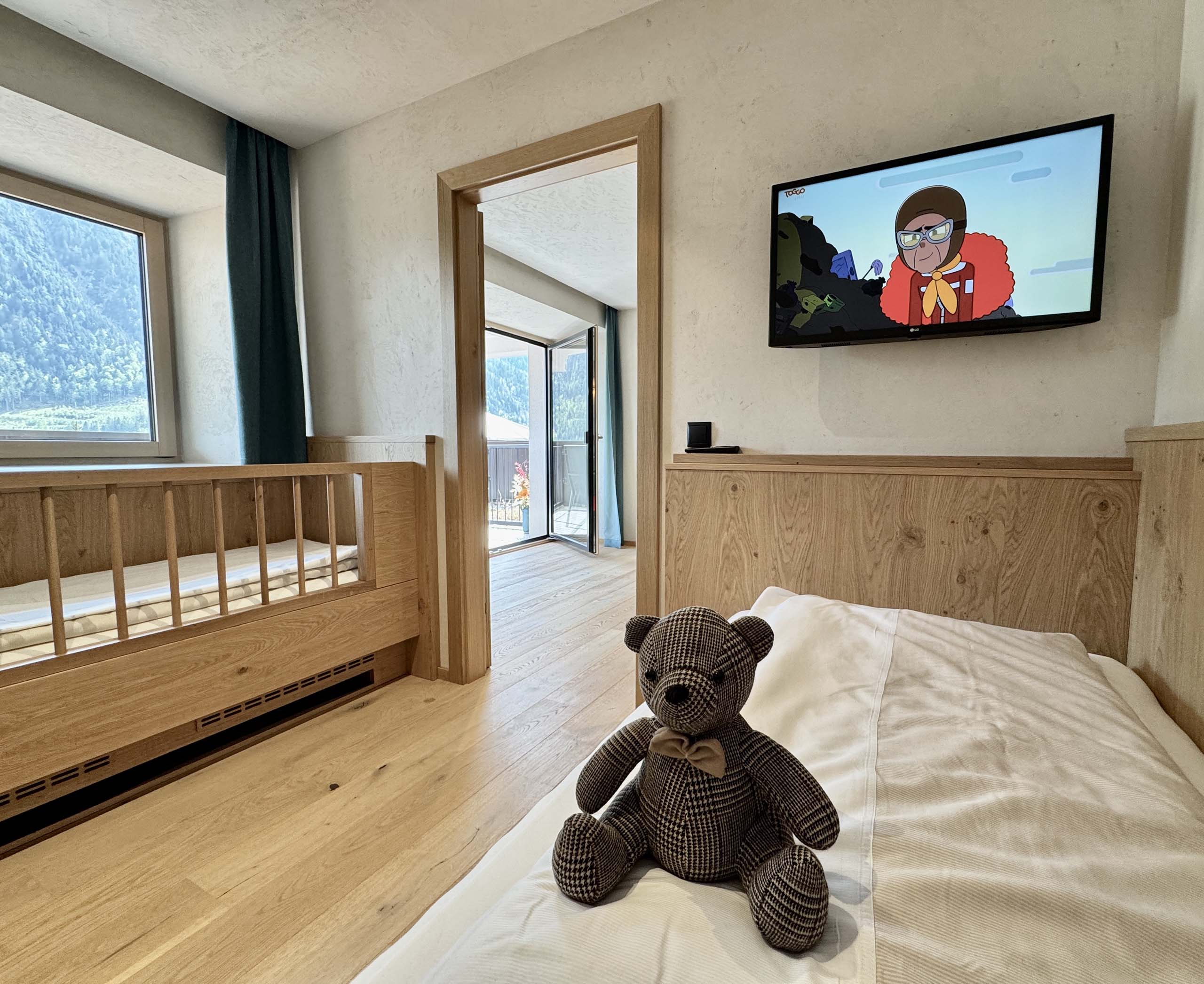Wir lassen Bilder sprechen. Kinderzimmer mit Holzmöbeln, Teddybär auf Bett und Fernseher an der Wand