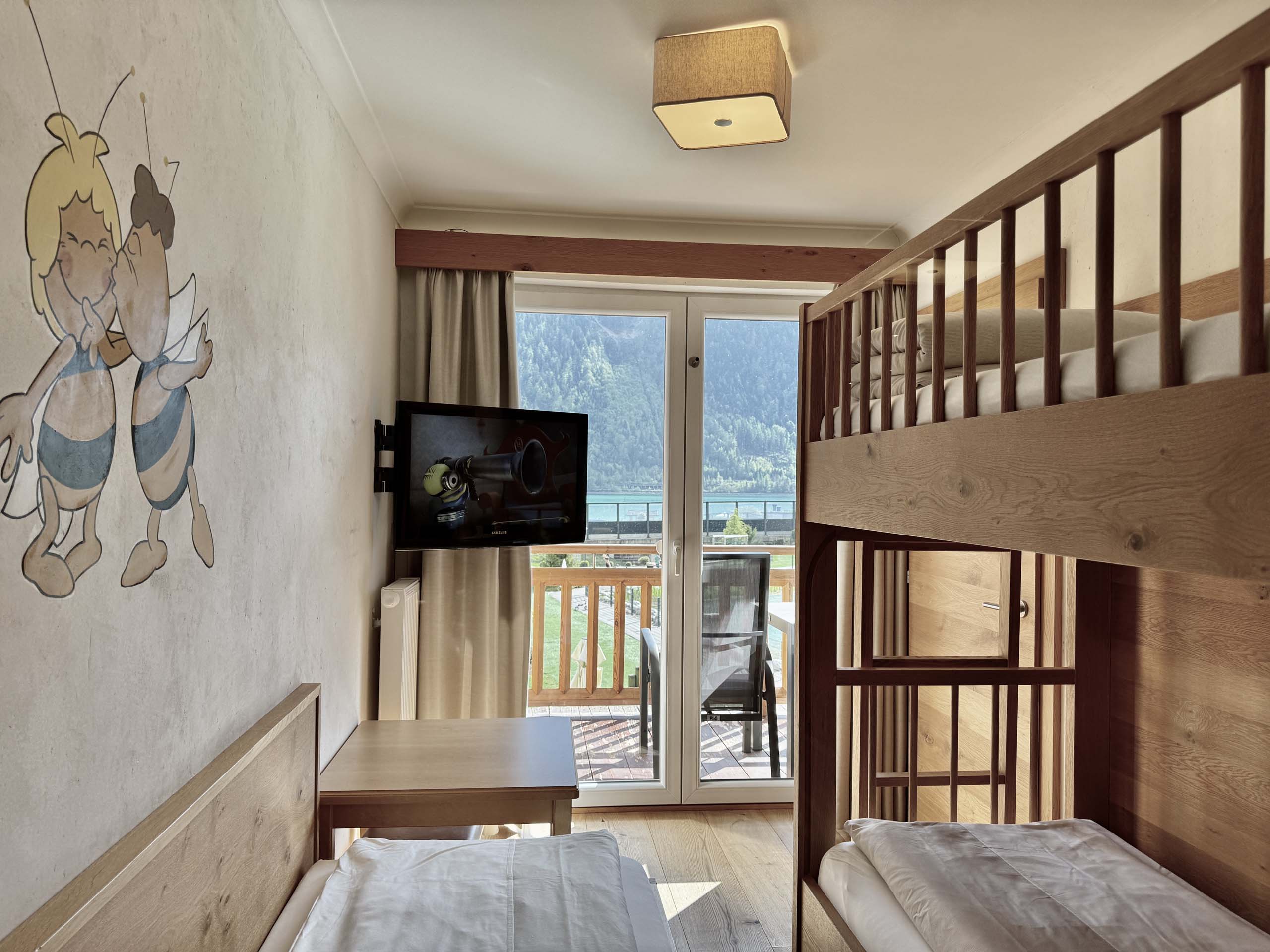 Wir lassen Bilder sprechen. Kinderzimmer mit Etagenbett, Einzelbett, TV und Balkon mit Bergblick