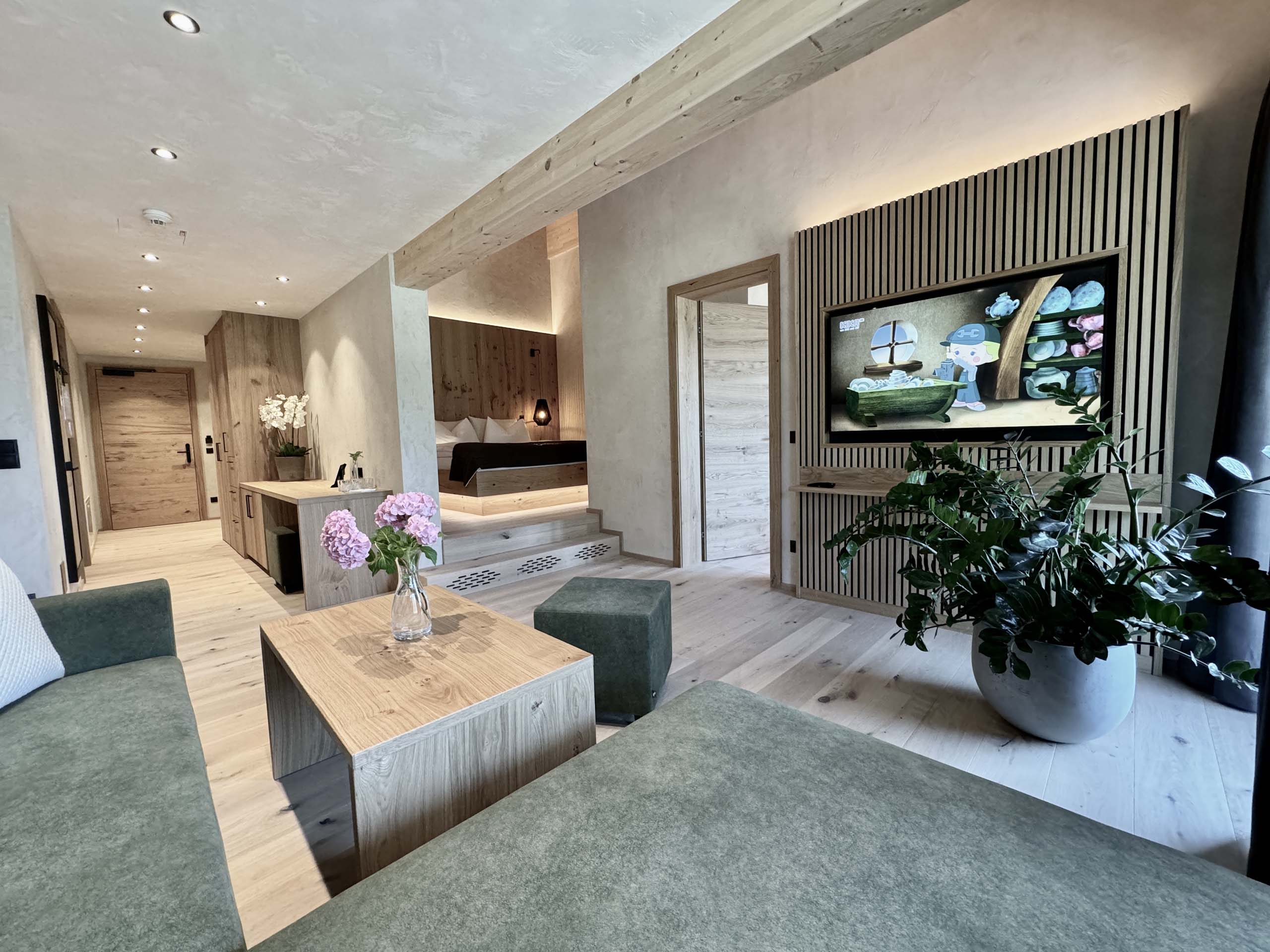 Wir lassen Bilder sprechen. Moderner Hotelzimmer-Wohnbereich mit grünem Sofa und Holzmöbeln