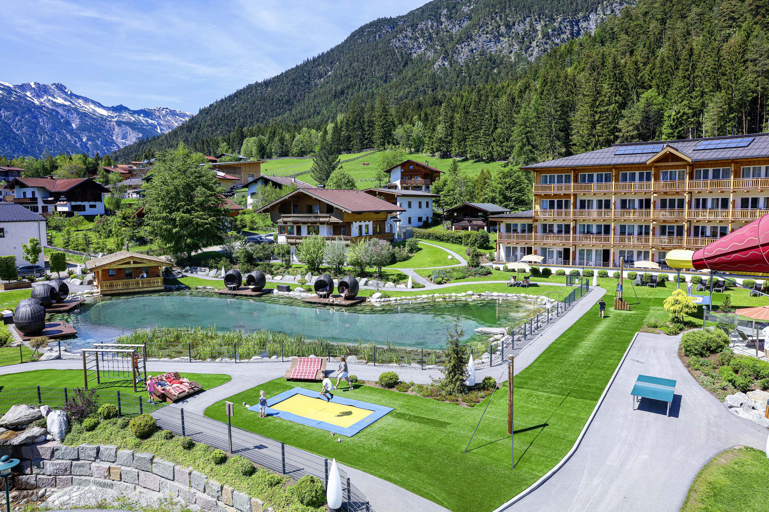 Wir lassen Bilder sprechen. Ferienanlage mit Naturbadesee, Spielplatz und Alpenkulisse im Hintergrund