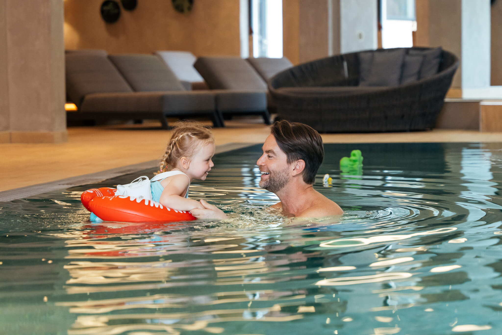 Wir lassen Bilder sprechen. Mann und Kind mit Schwimmring lächelnd und Händchen haltend im Hallenbad